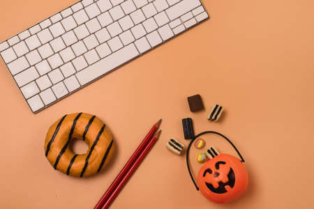 Holiday Halloween Home Office Workplace with Small Jack-O-Lantern Pumpkin Basket with Candy White Keyboars Red Pencils and Orange Donut Top View Flat Layの写真素材