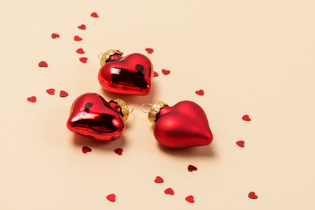 Three Christmas Ornaments in Shape of Hearts Red Decoration Ball Christmas or St. Valentine Background or Card Yellow Backgroundの写真素材