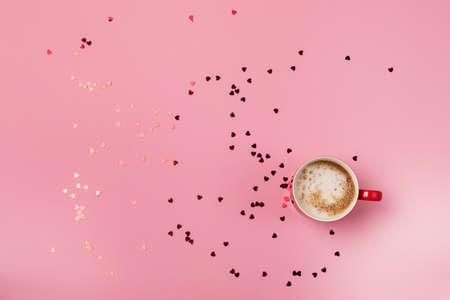 Red cup of coffee with cream and chaotically lying confetti in the shape of a heart St Valentine Background or Concept Top Viewの写真素材