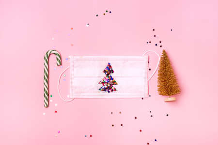 Christmas Concept Face Mask Decorated with Confetti Christmas decorations Candy Cane and Christmas Tree on pink background Top view Minimalismの写真素材