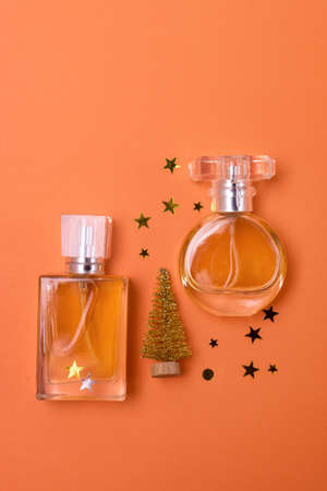 Different Perfume Bottles with Golden Christmas Tree and Golden Confetti on Orange Background Holiday Christmas Gift Concept Vertical Minimalの写真素材