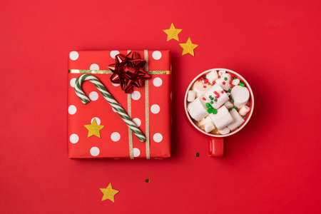 Christmas Gift Box and Red Cup of Hot Cocoa with Marshmallow Green Candy Cane Confetti Red Background Top Viewの写真素材