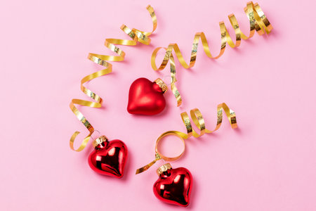 Three Red Heart Shaped Christmas Ornament with Golden Ribbon Pink Background Horizontal Christmas or St. Valentine Cardの写真素材