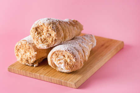 Three Tasty Homemade Pastry Tubes with Cream on Wooden Tray Pink Background Selective Focus Sweet Tube with Whipped Cream Close Upの写真素材