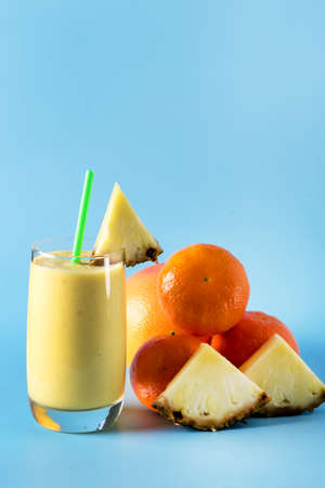 Freshly Blended Yellow and Orange Fruit Smoothie in Glass with Straw Pineapple and Citrus Smoothie Healthy Drink Blue Background Verticalの写真素材