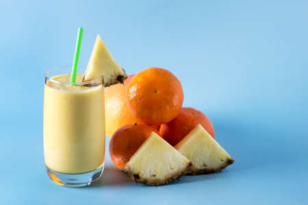Freshly Blended Yellow and Orange Fruit Smoothie in Glass with Straw Pineapple and Citrus Smoothie Healthy Drink Blue Background Horizontal Copy Spaceの写真素材