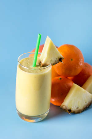 Freshly Blended Yellow and Orange Fruit Smoothie in Glass with Straw Pineapple and Citrus Smoothie Healthy Drink Blue Background Verticalの写真素材