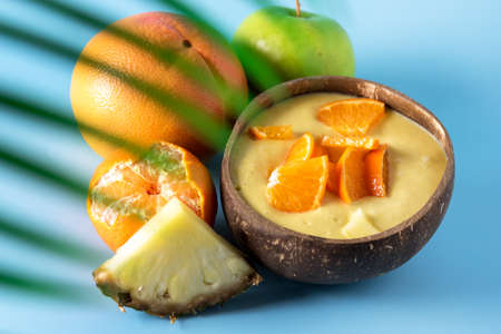 Healthy Smoothie from Banana Pineapple and Citrus in the Coconut Shell Bowl Healthy Summer Breakfast Blue Backgroundの写真素材