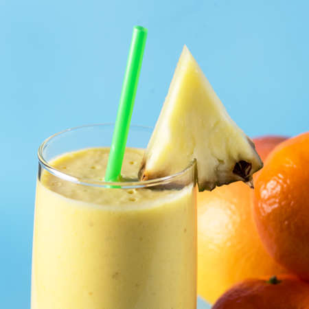 Freshly Blended Yellow and Orange Fruit Smoothie in Glass with Straw Pineapple and Citrus Smoothie Healthy Drink Blue Background Close Upの写真素材
