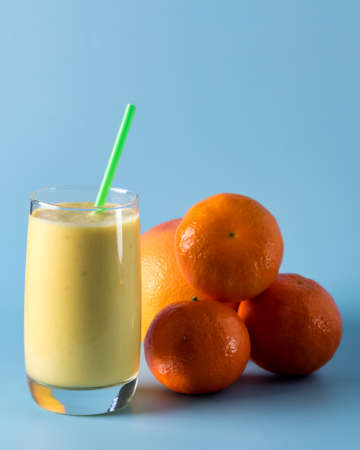 Freshly Blended Yellow and Orange Fruit Smoothie in Glass with Straw Pineapple and Citrus Smoothie Healthy Drink Blue Background Verticalの写真素材