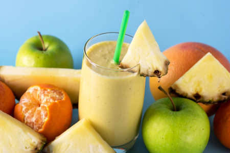 Freshly Blended Yellow and Orange Fruit Smoothie in Glass with Straw Pineapple and Citrus Smoothie Healthy Drink Blue Background Horizontalの写真素材