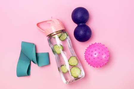 Bottle of Detox Healthy Water with Cucumber Fitness Band and Back Rollers Yoga and Pilates Concept Top View Pink Backgroundの写真素材