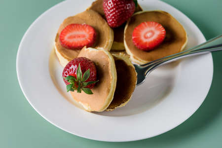 Dutch Mini Pancakes Called Poffertjes with Strawberry on White Plate Healthy Food Concept Green Backgroundの写真素材