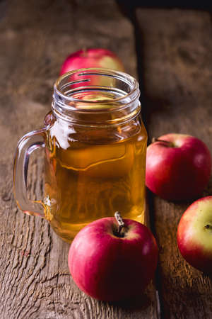 Glass Jar of Apple Juice with Red Apples on Old Wooden Background Vertical
