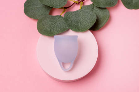 Women Health Concept Zero Waste Blue Menstrual Cup on Podium Fake Green Plant Leaves Background Alternative Reusable Product for Female Hygiene during Periods Minimalisの写真素材