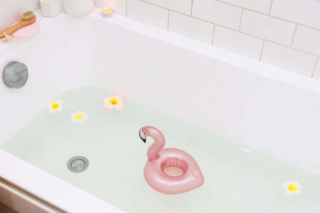 Bathtub with Plumerria Flowers and Inflatable Flamingo Toy Ring with Drink Bamboo Face Brush Home SPA Concept Relaxの写真素材