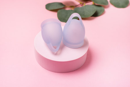 Women Health Concept Zero Waste Blue Menstrual Cup on Podium Fake Green Plant Leaves Background Alternative Reusable Product for Female Hygiene during Periods Minimalisの写真素材