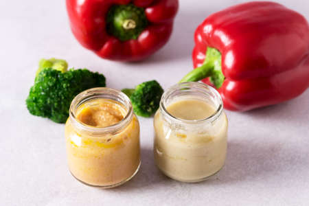 Glass Jars with Natural Baby Food on the Light Gray Background Vegetable Puree with Broccoli and Red Pepperの写真素材