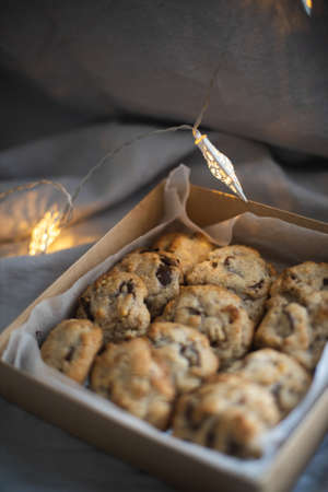 Box of chocolate chip cookies with Christmas lights behind, gray linen backgroudの写真素材