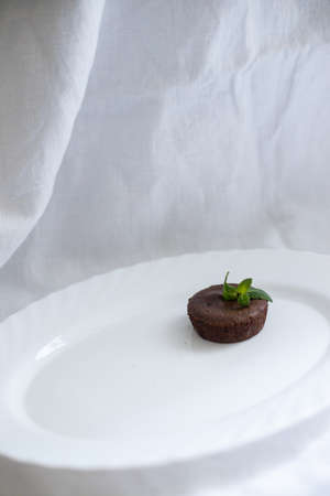 Minimalistic photo of chocolate brownie, with mint leaves, on white plate and white backgroundの写真素材