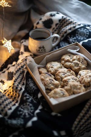 Box of cookies on a cozy Christmas pattern blanket near lights and cup of hot drinkの写真素材