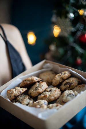 Woman holds a box with chocolate chip cookies, Christmas tree behind with lights and sparklesの写真素材
