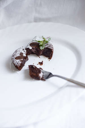Chocolate fondant cut in half with a spoon on white oval dish with mint leaves onの写真素材