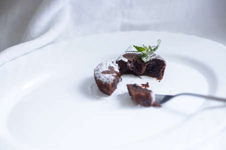 Chocolate fondant cut in half with a fork on white oval dish with mint leaves onの写真素材