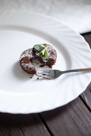Vertical photo of chocolate fondant cut in half with a fork on white oval dish with mint leaves onの写真素材