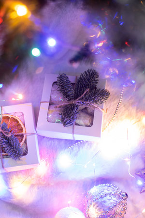 A small Christmas gift box decorated with fir branch, laying on fur cloth, led neon lights and tree behindの写真素材