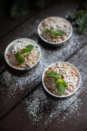 Vertical image of three festive cupcakes with mint leaves and powdered sugar decoration standing on dark wooden tableの写真素材