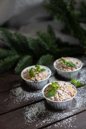 Vertical image of three festive cupcakes with mint leaves and powdered sugar decoration standing on dark wooden table and fir branch behindの写真素材