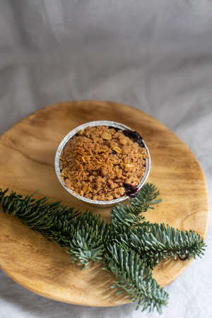 Closeup shot of crumble cake in a small cup placed on wooden plate decorated with fir branchの写真素材