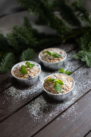 Vertical image of three festive cupcakes with mint leaves and powdered sugar decoration standing on dark wooden table and fir branch behindの写真素材