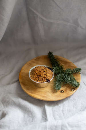 Crumble cake in a small cup placed on wooden plate decorated with fir branchの写真素材