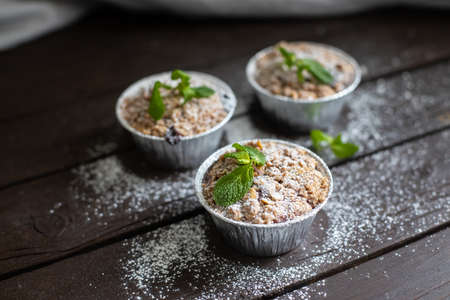Small cupcakes with mint leaf decoration standing on dark wooden table and powdered sugar sprinkled aroundの写真素材