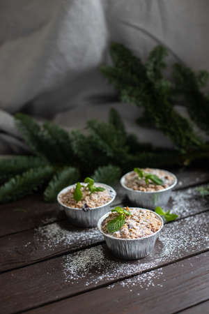 Vertical image of three festive cupcakes with mint leaves and powdered sugar decoration standing on dark wooden table and fir branch behindの写真素材