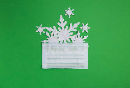 Christmas themed flat lay shot with medical mask on green background with snowflakes showing up from behind the maskの写真素材
