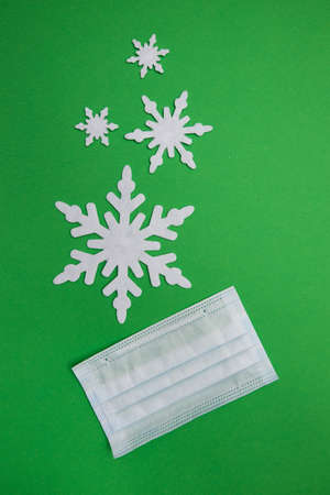 Vertical shot of medical mask on green backdrop with white snow flakesの写真素材