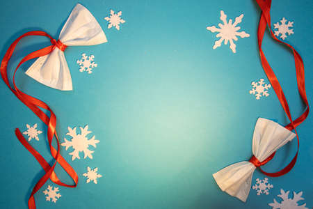 Frame with Christmas decorations made out of medical masks laying on blue backdrop with red ribbons and white snowflakesの写真素材