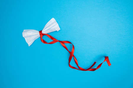 Coronavirus medical mask Christmas decoration with red ribbon and blue backdropの写真素材