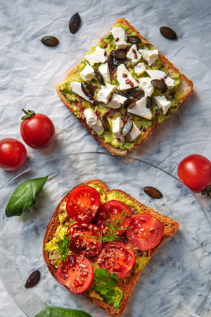 Savor the perfect combination of creamy guacamole, tangy feta cheese, and juicy sliced cherry tomatoes on toast.の写真素材