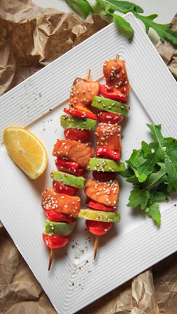 skewers of salmon, zucchini and tomato on a square plate on craft paperの写真素材