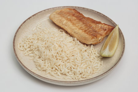 Grilled cod fillet with rice and lemon wedge on ceramic plate, top view.の写真素材