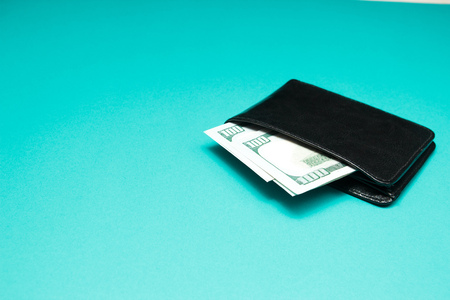 Black leather wallet with dollar bills on blue background. Men's purse with money bills.