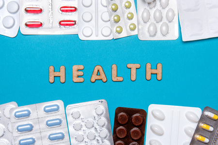 Pills with wooden letters form the word health on a blue background. Top view.