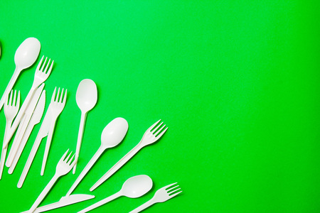 White single-use plastic knives, spoons, forks on a green background. Say no to single use plastic. Environmental, pollution conceptの写真素材