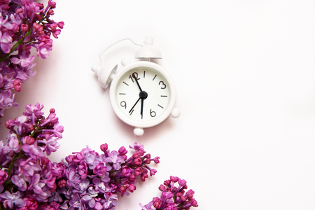 Lilac flowers with vintage tiny alarm clock on white background. Spring morning concept. Top view, flat lay.の写真素材