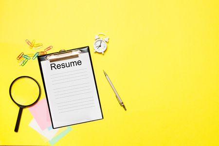 Resume with office supplies on a yellow background. Concept of new job, hiring recruitment process, new team members screeningの写真素材