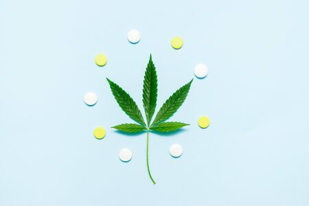 Marijuana leaf with medical pills on blue background. The concept of legalization of marijuana. Top...